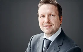 Porträt eines Mannes in einem Anzug mit einem neutralen Hintergrund.