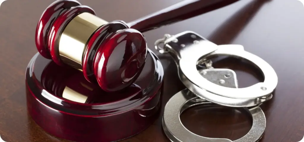 Ein Richterhammer aus Holz und eine silberne Handfessel auf einem Tisch.