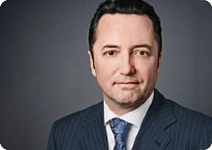 Porträt von Acun Ilıcalı in einem Anzug mit gestreifter Krawatte vor einem neutralen Hintergrund.