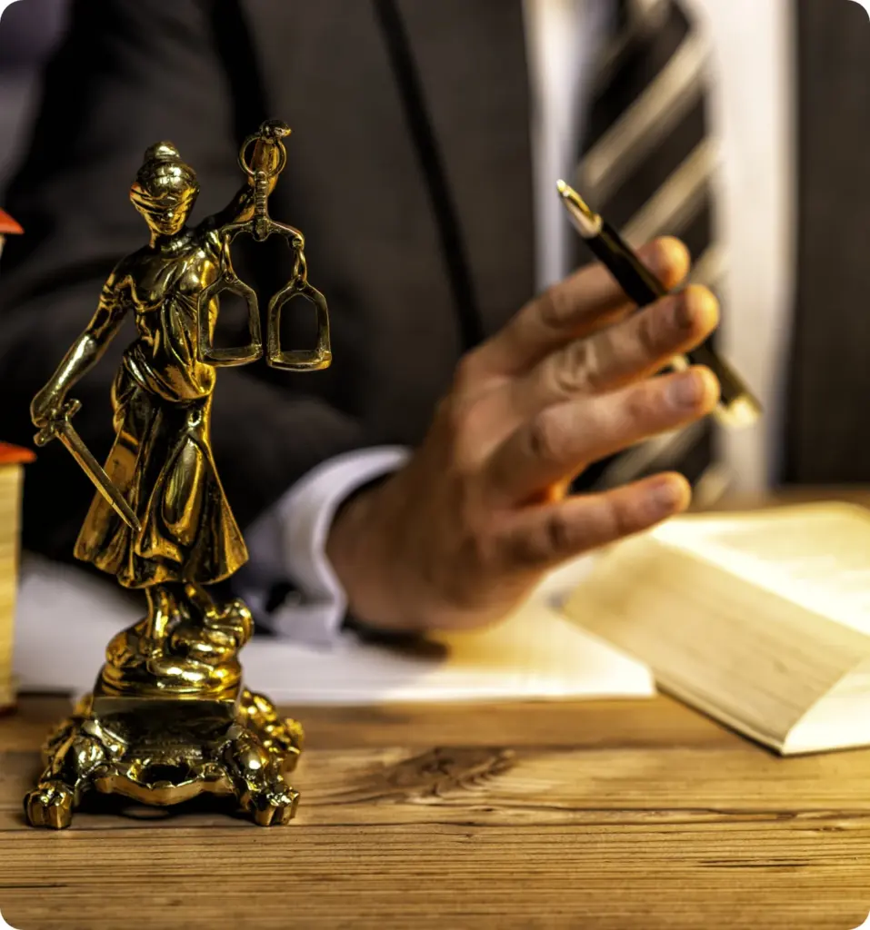 Goldene Justitia-Statue mit Waage und Schwert, dargestellt auf einem Tisch neben einem Buch.