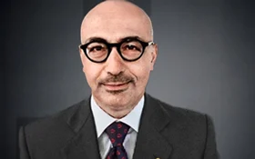 Porträt eines Mannes mit Brille, Anzug und Krawatte vor einem neutralen Hintergrund.