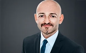 Porträt eines Mannes mit Glatze und Anzug, der in die Kamera lächelt.