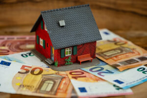 Ein Miniaturhaus, welches auf einem Grund bestehend aus Geld steht.