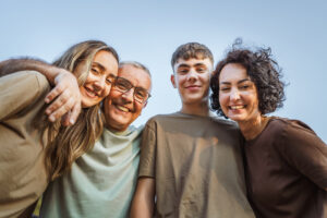 Eine Familie bestehend aus vier Personen, die vertraut in die Kamera lächelt.
