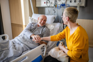 Eine Frau, die am Bett eines Mannes sitzt und seine Hand hält.
